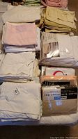 Stack of folded sheets, pillowcases, and linens in various colors including cream, pink, and white, some packaged