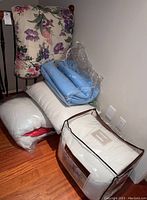 Photo of floral-patterned comforter, blue comforter, white pillows and bed linens stacked on floor