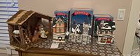 Photo showing three Dickensville light-up buildings and a ceramic Nativity set arranged on a table, some with original packaging visible.
