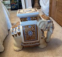 Side view of ceramic elephant plant stand showing detailed blue and brown patterns and cream base.