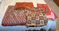 Four woven fabrics laid out on bed with varying international and horse-themed patterns