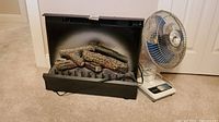 Electric fireplace insert and Panasonic fan side by side on carpeted floor.