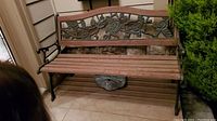 Full view of the garden bench showing wooden slat seat and wrought iron frame with floral backrest decoration.