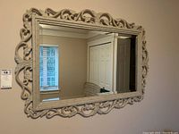 Front view of the wall mirror mounted on the wall showing the ornate molded resin composite frame and reflective surface.