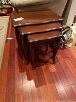 Set of three stacked wooden nesting tables showing size gradation and profile view of curved legs.