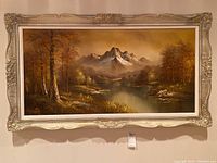Full front view of framed landscape painting showing mountain, lake and trees within ornate silver decorative frame