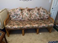 Front view of three-seat rattan sofa with floral cushions arranged on a beige carpet in a room.