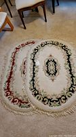 Two oval hand knotted Oriental wool rugs side by side, showing complimentary floral patterns and fringed edges.