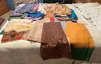 Scarves laid out on bed showing variety in colors and patterns, including floral and solid color pieces