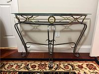 Front view of the demilune side table showing black metal frame with gold circular accents and curved legs, glass top resting on frame.