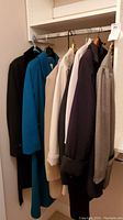 Six women's coats and jackets hanging on a clothing rod in a closet, showing variety of colors and styles.