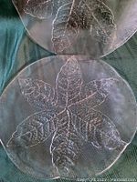 Two clear glass vintage Kosta Boda platters with embossed leaf pattern laid on dark green fabric, showing detailed texture and design.