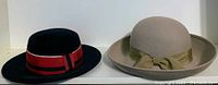 Two hats shown side by side: the black hat with red and black band, and the beige hat with matching band and bow.