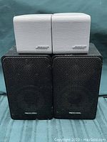 Front view showing white Bose speakers on top and black Realistic speakers beneath them, highlighting brand logos and grill designs.