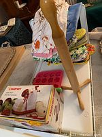 Photo showing wooden-handled apple peeler, pink candy mold, and cloth aprons.