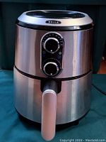 Front view of Bella air fryer showing stainless steel body and dual control knobs for temperature and timer.