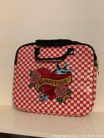Front view of padded laptop bag showing red and white checkered pattern and embroidered Betseyville logo patch with roses and birds