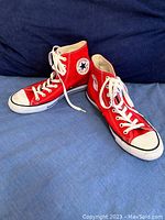 Pair of red Converse Chuck Taylor high top sneakers showing both shoes on a blue background.