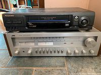 Front view of Panasonic VCR stacked on JVC stereo receiver showing front controls and cassette slot.