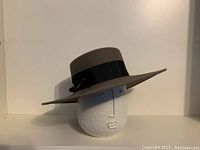 Full side profile of taupe fur felt ladies hat on white mannequin head showing wide brim and black grosgrain ribbon band with decorative hatpin.