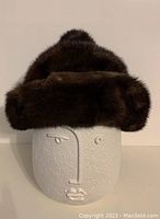 Front view showing the dark brown thick mink fur hat with pom pom topped crown and folded brim on a white mannequin head.