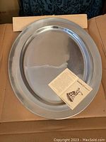 Top view of large silver-colored oval tray with semi-matte finish, showing smooth surface and informational paper laid in center.