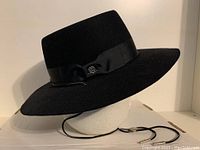 Black cowboy hat displayed on a white mannequin head showing side view with leather chinstrap and metal bolo tie closure visible.