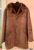 Front view of the brown suede winter coat showing button closure, front pockets, and collar.