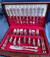 Wooden case open showing felt-lined interior with flatware arranged