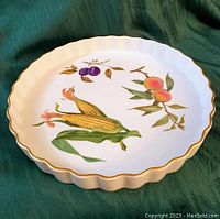 Top-down angled photo showing detailed Evesham fruit and vegetable pattern on fluted edge ceramic dish with gold trim
