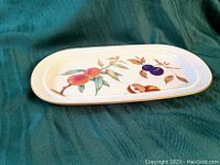 Close-up photo of the rectangular dish showing colorful fruit design of peaches and plums with gold trim on a white porcelain base.