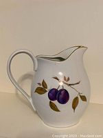 Front view of water jug showing purple plum fruit pattern with leaves and gold rim on spout.