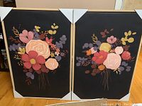 Two framed prints featuring colorful floral bouquets framed in light wood, corners protected by white cardboard.