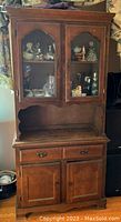 Full view of the vintage maple buffet cabinet with upper glass doors displaying decorative items, and the lower section with drawers and closed doors.