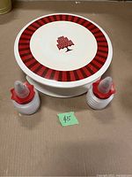 Full view of the 12-inch rotating cake stand with red and white striped design and cake graphic in center, alongside two Betty Crocker decorating bottles with red lids.