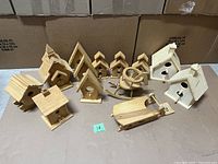Photo showing all 13 wooden craft items arranged on a cardboard surface, including several small birdhouses in natural wood finish and a wooden rocking chair shape.