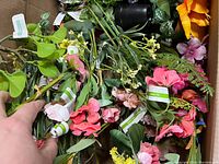 Top view of a box containing assorted artificial flowers in pink, green, and yellow colors with visible stems.
