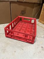 Photo showing full rectangular red plastic Coca-Cola bottle tray with cutouts on sides and base, positioned on concrete floor.