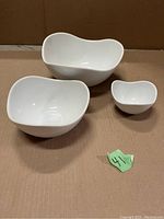 Three white nesting bowls placed side by side on cardboard with small green lot number tag.