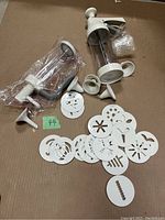 Pampered Chef cookie press laid out with multiple shaping discs and attachments on cardboard surface.