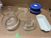Photo showing a variety of Pyrex clear glass bakeware including round, oval, and ribbed-bottom dishes, white ceramic rectangular dish, and two blue plastic lids.