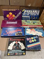 Photo of seven vintage board game boxes arranged for sale: Quick Wit, Entertainment Trivia, Superstations, Monopoly, Jeopardy!, Tour de Force, Kensington game