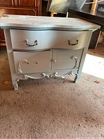 Front view of antique wooden cabinet showing detailed drawers and door with metal and knob handles. Partial paint removal on top surface visible.