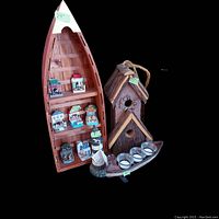 Photo showing the wooden canoe-shaped shelf holding seven Baileys limited edition scene figurines, the wooden bird house with rope handle, and the wooden lighthouse candle holder with four candle spots.