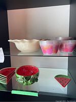 Display of bowls and plates on shelves including watermelon-themed ceramic items and plastic floral bowls.