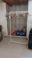 White metal extendable clothes rack with some wooden and plastic hangers hung on it, missing some plastic floor protectors on feet.