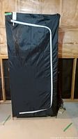 Front view of black covered clothes storage unit with white zipper, fully closed.