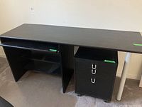 Black laminate desk showing long desktop surface with an open shelf and attached side panel, keyboard drawer present underneath the surface.