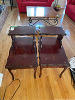 Four wooden end tables shown from above and front angle, placed on wood floor. Tops have heavy wear and scratches, upper shelves supported by legs visible.