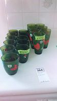 Eighteen green plastic glasses arranged in two rows, showing red strawberry and white flower patterns.